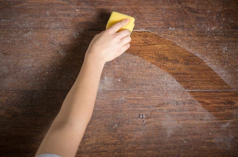 Yellow sponge is being used by a hand for cleaning dusty wood