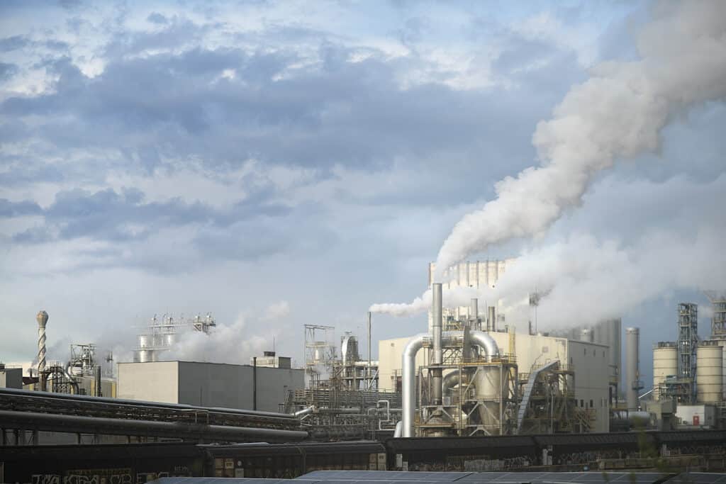 Industrial plant with tall smokestacks releasing steam or smoke into a cloudy sky