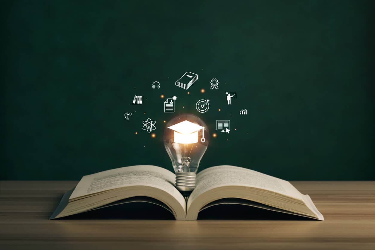 Lightbulb on a book with graduation hat, and education icons
