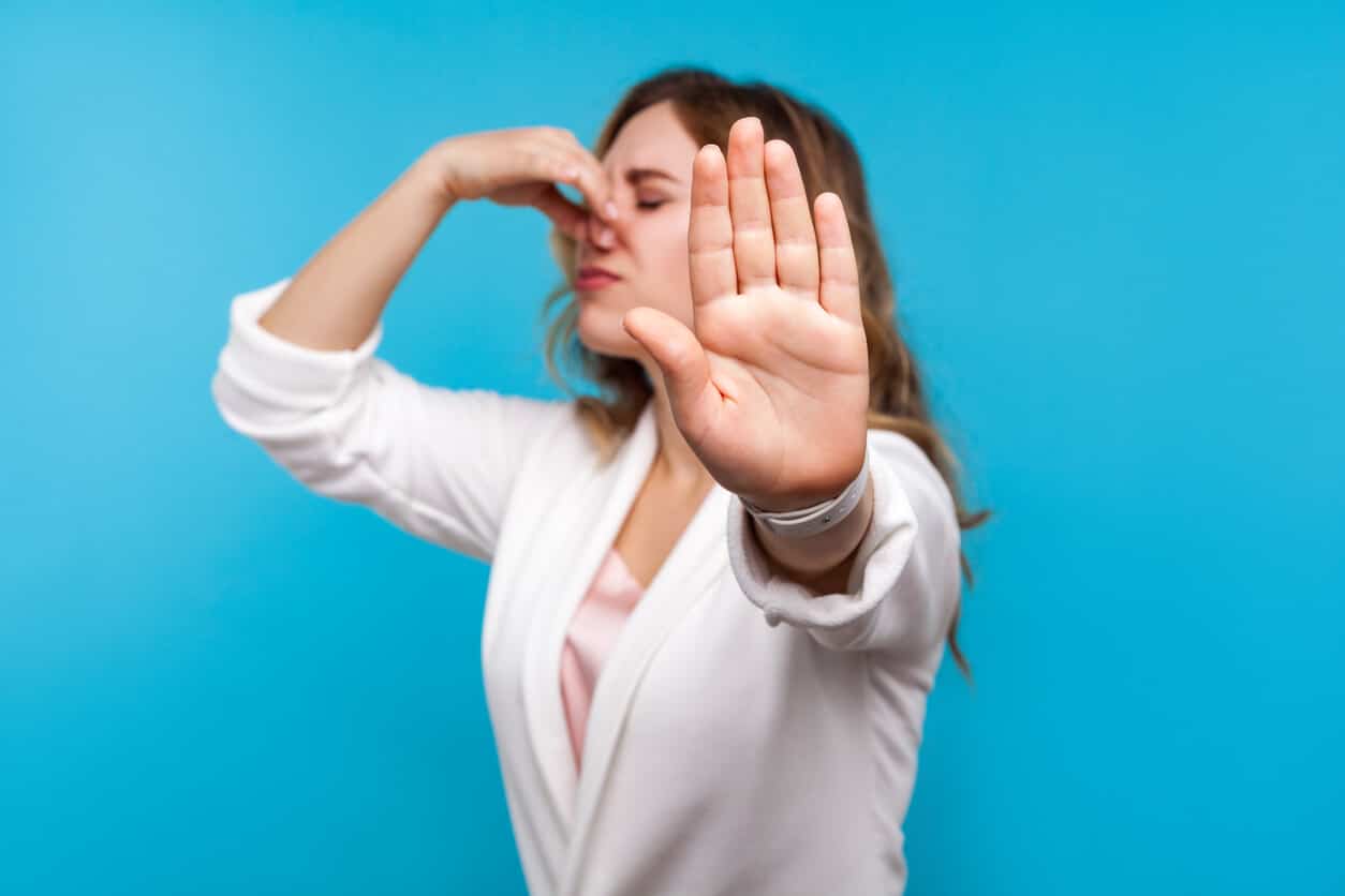 Bad smell. Woman with wavy hair in white jacket pinching her nose and showing stop gesture, expressing disgust to unpleasant odor.